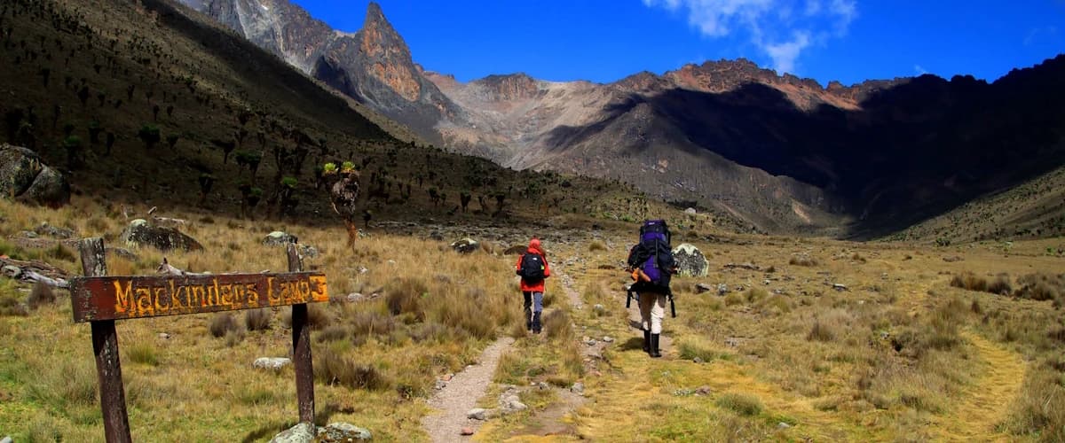 Two trekkers with backpacks beside a Mackinder's Camp trail sign