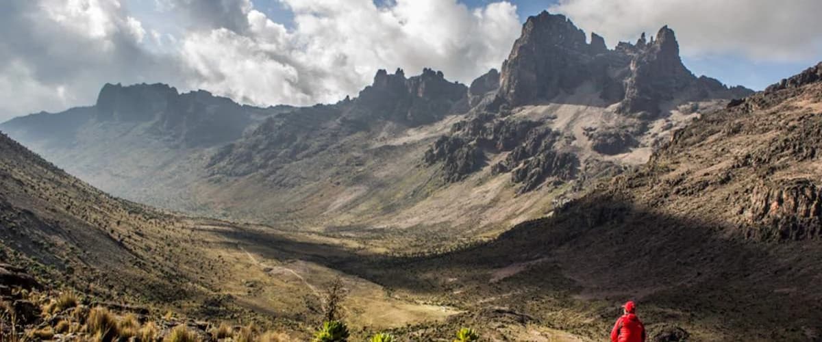 Distant trekker walking through a broad mountain valley beneath steep slopes