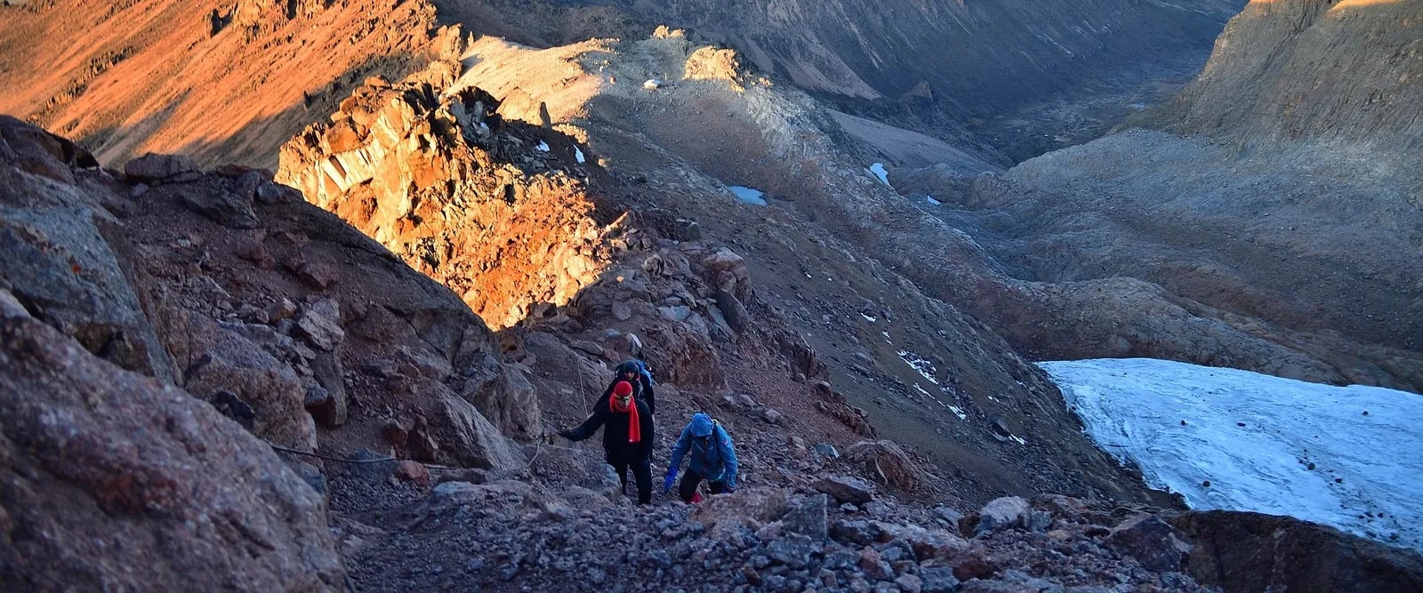 Two trekkers with backpacks crossing rocky mountain terrain